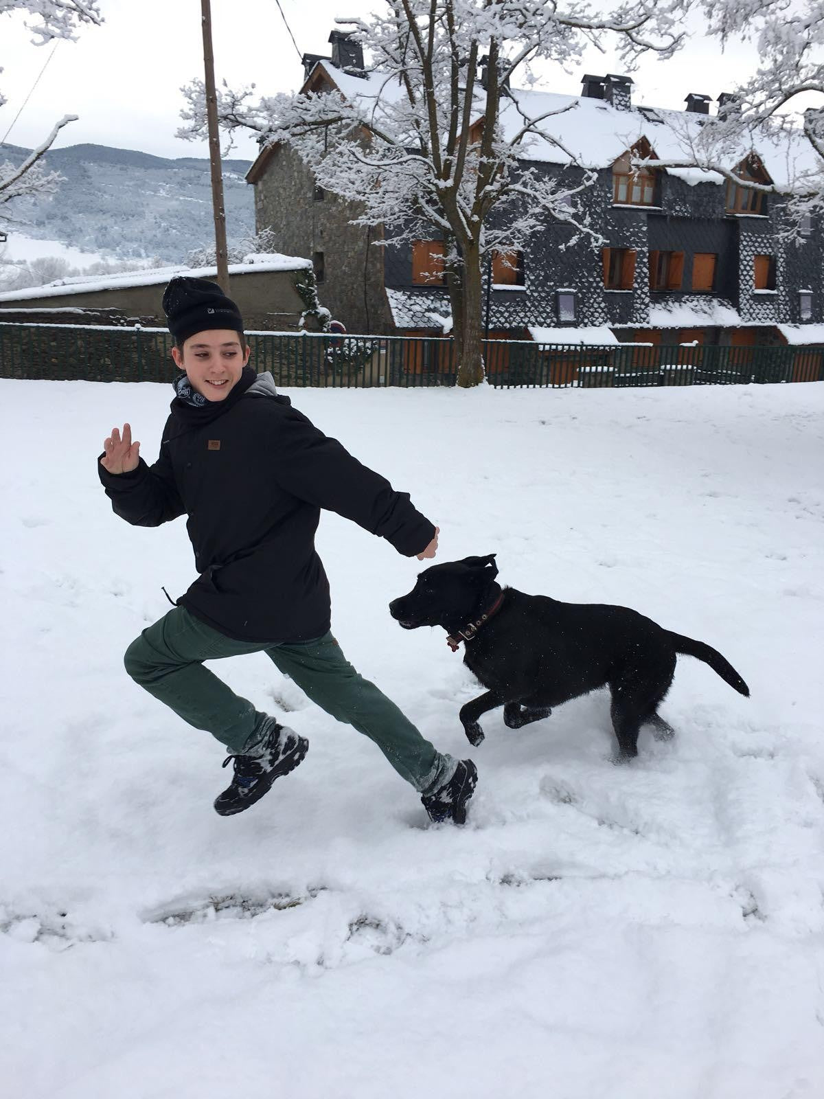 Hugo corriendo por la nieve con Ray, su labrador negro, detrás